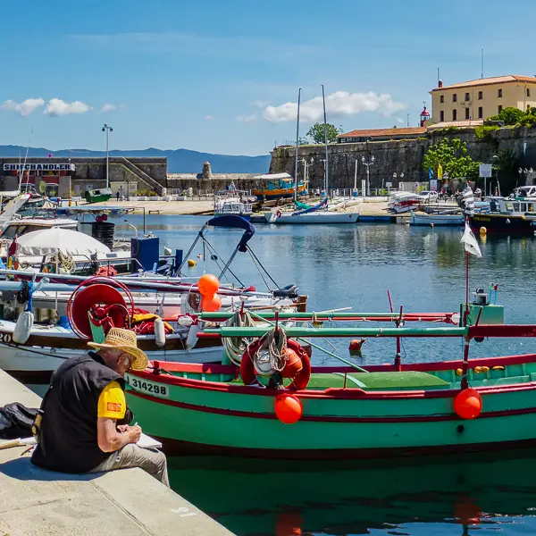 A man sits at a marina in Corsica.