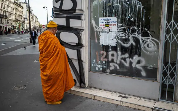 A Buddhist monk contemplates a vacant storefront in Paris, France.