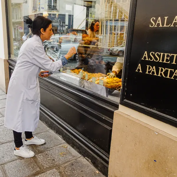 A foodservice worker in Paris signals to a clerk inside a bakery.