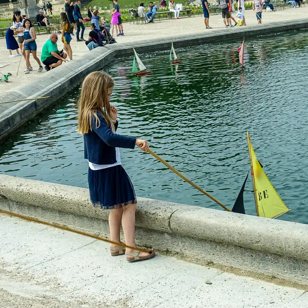 A girl steers a model sailboat on a pond in the Jardin du Luxembourg.