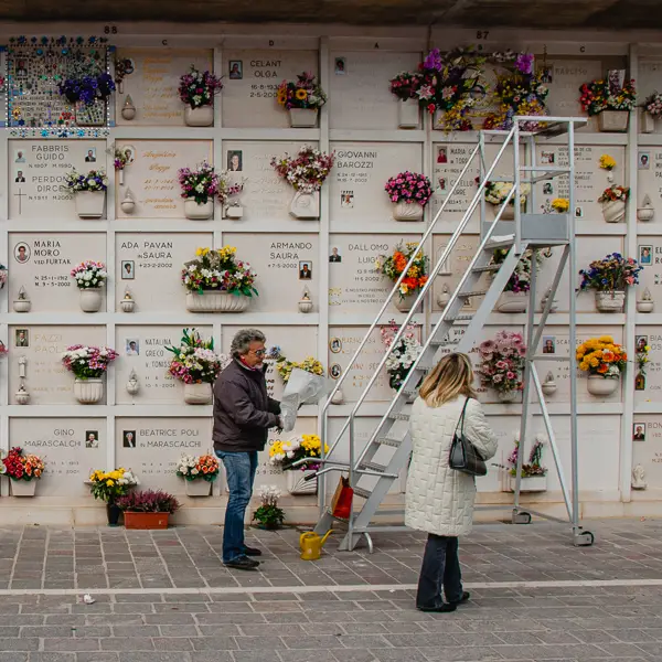 A man and a woman use a rolling ladder to place flowers on a mausoleum niche in San Michele's Catholic section.