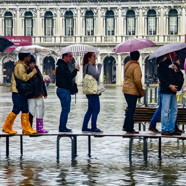Pedestrians cross passerelle (raised walkway sections) in Venice's Piazzale Roma during 'acqua alta' or tidal flooding.