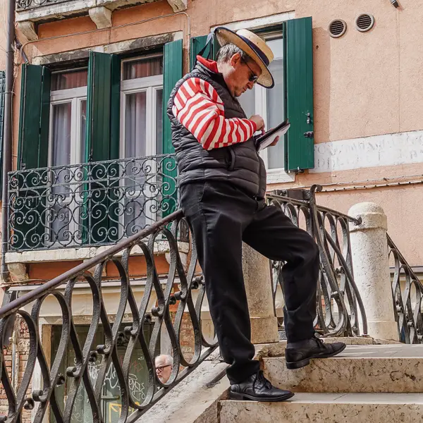 A gondolier checks his phone while waiting for customers.