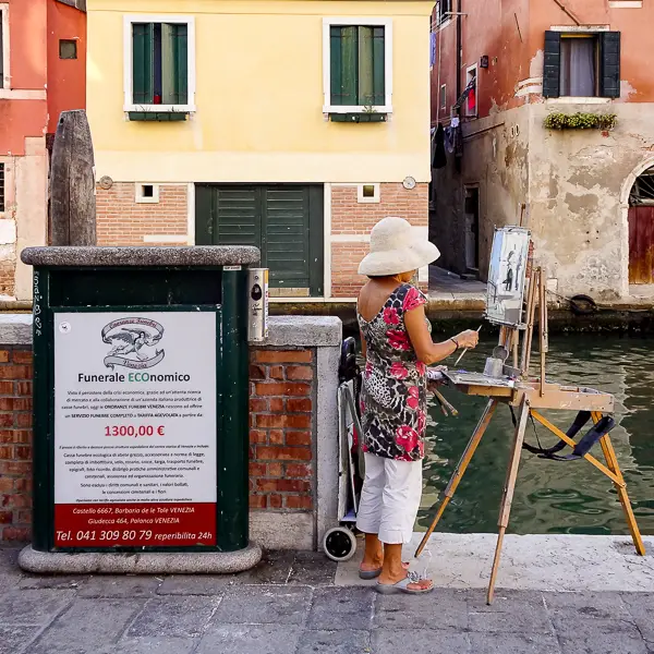 An artists paints a scene next to a trash can with a poster for cheap funerals.