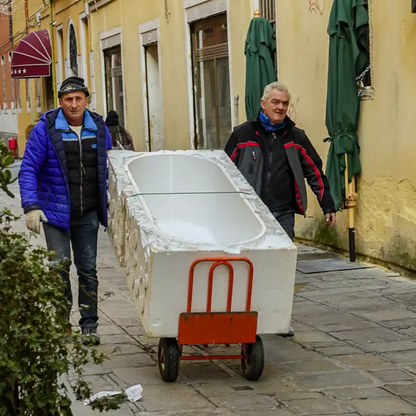 Delivery men wheel a bathtub along a street in Venice, Italy.