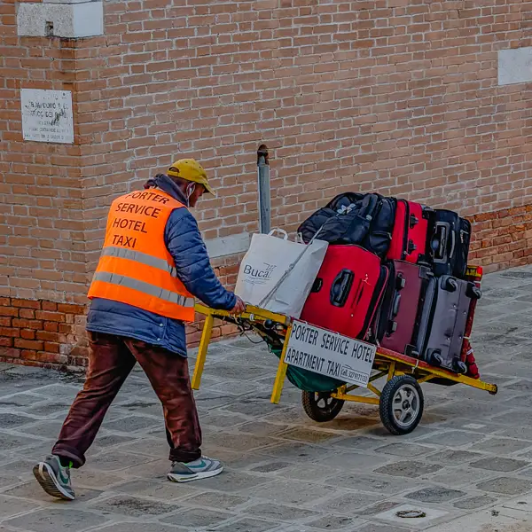 A baggage porter rolls a cartload of suitcases to a Venice hotel.