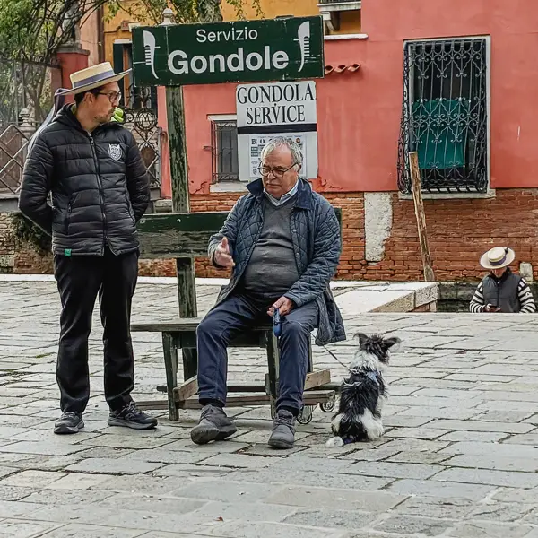 A gondolier in Venice, Italy chats with a man and his dog.