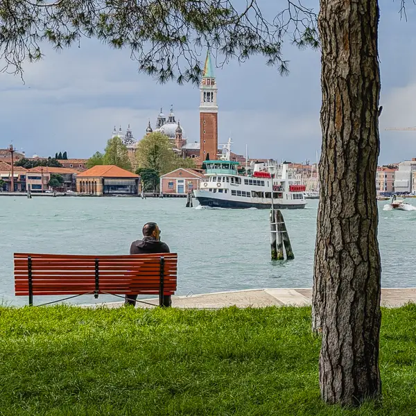A man watches from a park bench as a public water bus heads from central Venice to islands of the Venetian Lagoon.