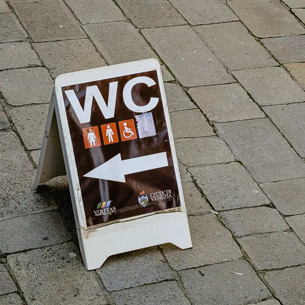 A sandwich sign points to municipal toilets in Venice's historic center.