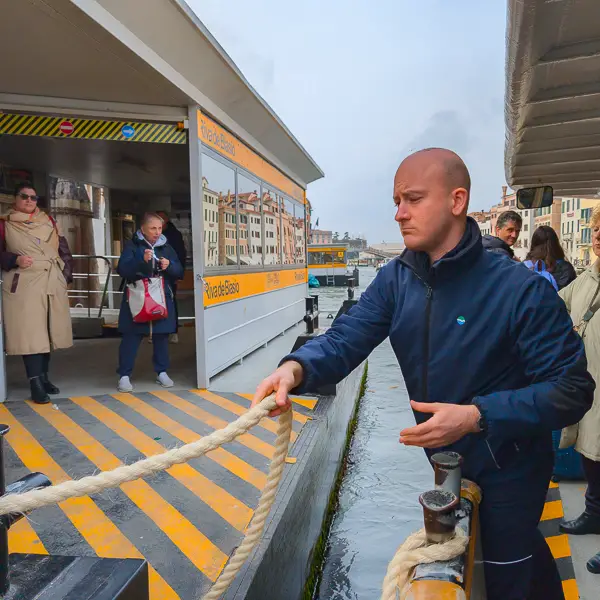 A sailor uses a mooring line to secure a vaporetto (water bus) on Venice's Grand Canal.