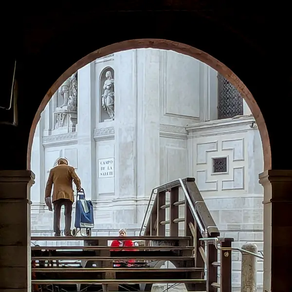 A man carries his shopping cart over a bridge next to the Basilica di Santa Maria della Salute in Venice, Italy.